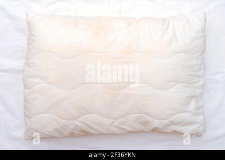 Old used white pillow with stains on crumpled sheet, dirty pillow on the bed Stock Photo