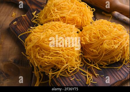 Fresh Tagliatelle pasta . Traditional Italian named Angel Hair . capellini d'angels. Woman cooking Italian egg pasta, homemade and fresh in flour on a cutting table.  Stock Photo