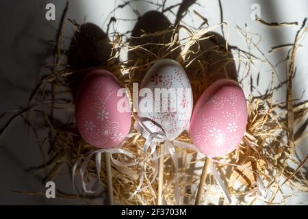 Two pink eggs and one white in the hay, beautiful background with shadows Stock Photo