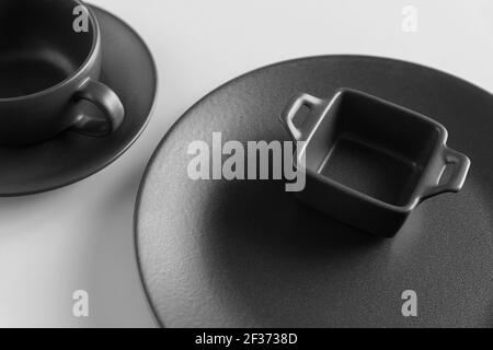 Black empty plates, cup and saucer and small baking dish on white background Stock Photo