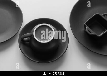 Two black empty plates, an inverted cup and saucer and a small baking dish on a white background Stock Photo