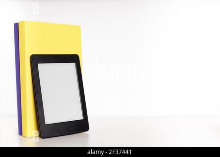 Yellow and purple books with blank spine and an electronic reader on a white shelf with white background. Concepts of technology, reading and educatio Stock Photo
