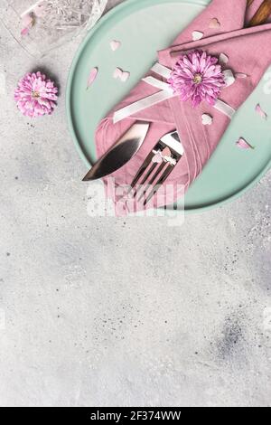 Beautiful festive table setting with green plate, napkin, flowers and hearts decoration on gray stone background. Top view with copy space. Stock Photo