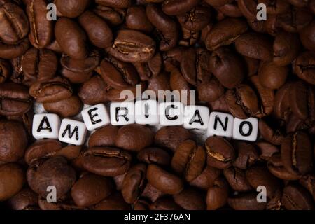 close up of Freshly roasted coffee beans near word AMERICANO written with little white cubes. top view. Stock Photo