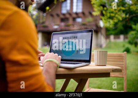 Unrecognizable man with laptop working outdoors in garden, home office concept. Stock Photo