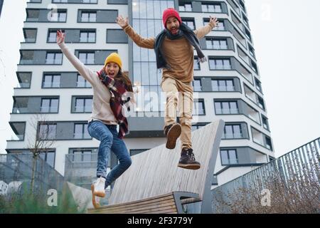 Cheerful young couple owners jumping outdoors in front of new flat, new home and relocation concept. Stock Photo
