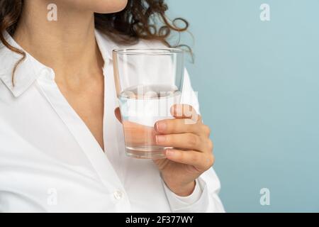 Woman holding drinking water glass in her hand isolated on studio blue background. Healthy lifestyle Stock Photo