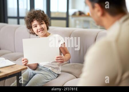 Happy latin boy showing the drawing to his dad while spending time with his father, playing in the living room at home Stock Photo
