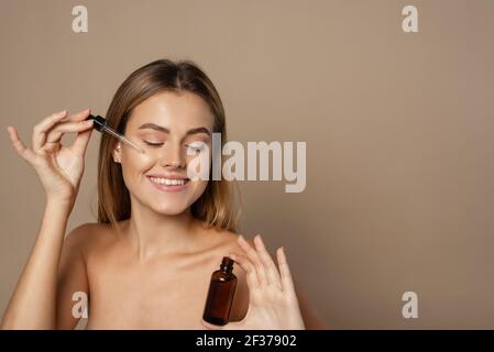 Beautiful face portrait of young woman is applying face serum on a cheek. Stock Photo