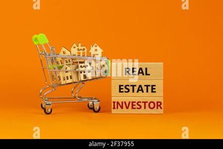 Real estate investor symbol. Wooden blocks, words 'Real estate investor' on beautiful orange background. Shopping cart with miniature wooden houses. B Stock Photo