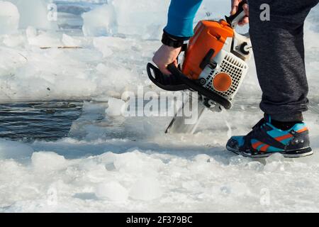 a man with a chainsaw cuts the ice on the lake Stock Photo