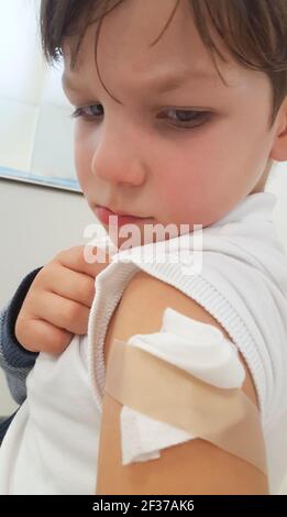 Sad and in pain child boy shows his arm after vaccination. Selective focus Stock Photo