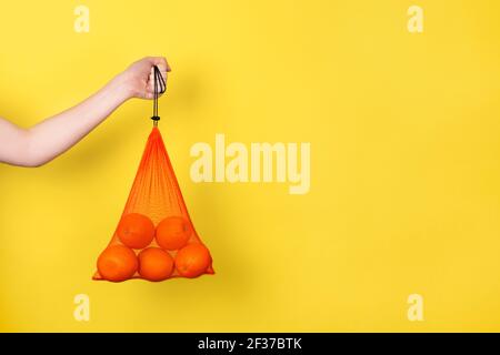 Female hand holding Oranges in eco bag for grocery isolated on yellow. Eco friendly Shopping Bag concept. Banner with copy space Stock Photo