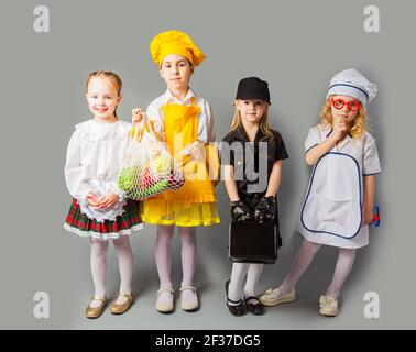 Happy schoolgirls in costumes of different professions isolated on grey Stock Photo