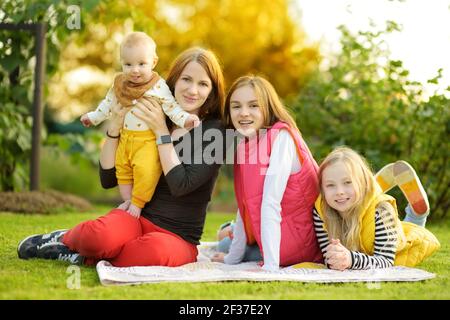 Mother and three children having fun on autumn day in city park. Adorable baby boy being held by his mommy. Two older sisters hugging their mom and ba Stock Photo