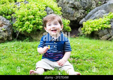 little boy sitting in the grass holiding a leaf Stock Photo