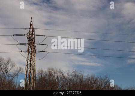 Overhead electrical power lines on a transmission tower against white and blue sky background Stock Photo