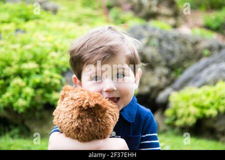 little boy playing with a teddy bear in the garden Stock Photo