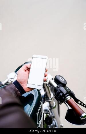Man holding smartphone while sitting on vintage motorbike Stock Photo
