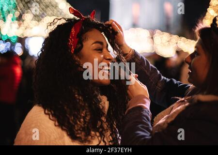 Happy young woman standing with girlfriend in city during christmas Stock Photo