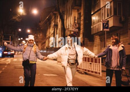 Happy female friends holding hands walking on road in city at night Stock Photo