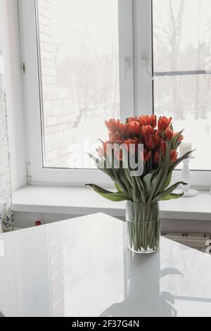 a bouquet of tulips in a transparent vase on a white table against the Stock Photo