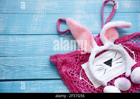 easter composition with easter bunny ears, medical mask, eggs and string bag. Stock Photo
