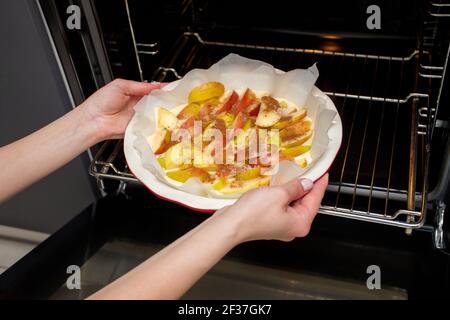 The hostess prepares apple charlotte at home in the kitchen and puts in the oven an apple pie Stock Photo