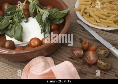 Close-up of a table where an Italian pasta recipe is being prepared with cherry tomatoes, cheese and fresh basil leaves Stock Photo