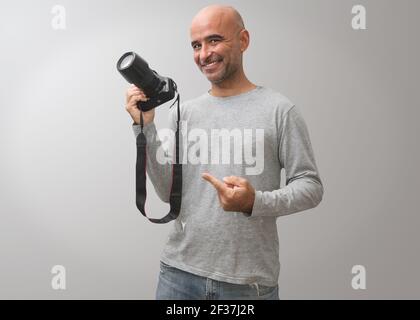 A Hispanic bald man smiling and pointing at his camera on a gray background Stock Photo