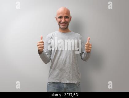A Hispanic bald man smiling and showing his thumbs on a gray background Stock Photo