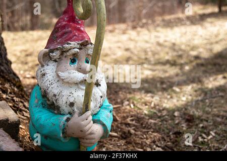 Gnome, lawn ornament, white beard blue eyes, ceramic, weathered, paint chipping, gold yellow staff, red hat, white, turquoise blue jacket, cute, frien Stock Photo