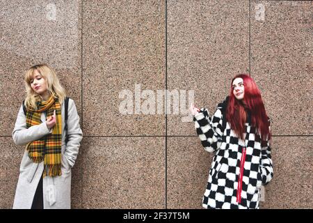 Two young women are cursing. Quarrel, aggression, stress. Two brunette girlfriends swear. Scream. Point fingers to the head. An emotional solution to Stock Photo