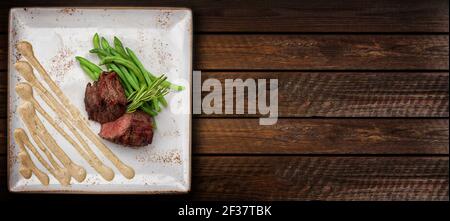Filet mignon on a white square plate with asparagus and sauce. Horizontal wooden background Stock Photo