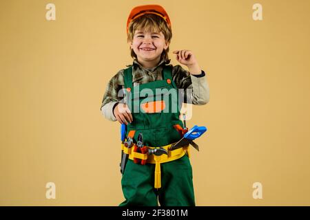 Little repairman. Kid boy in builders uniform and helmet with repair tools. Child game. Little boy plays construction worker. Stock Photo