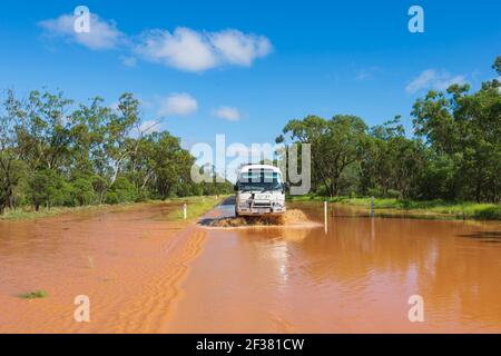 Toyota Coaster mini-bus driving through floods on a remote Outback road covered in red mud after a storm, near Thallon, Queensland, QLD, Australia Stock Photo