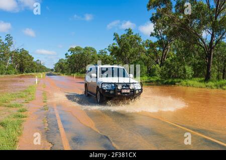 A car driving through floods on a remote Outback road covered in red mud after a storm, near Thallon, Queensland, QLD, Australia Stock Photo