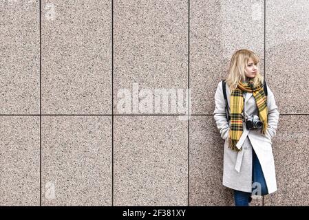 a blonde woman with a retro camera stands against the wall and looks away. free space. copy space Stock Photo