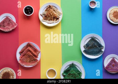Rainbow pancakes, different color crepes. Spinach, beetroot powder, blue matcha and turmeric crepes. Colorful pancakes, flat lay on rainbow layered Stock Photo