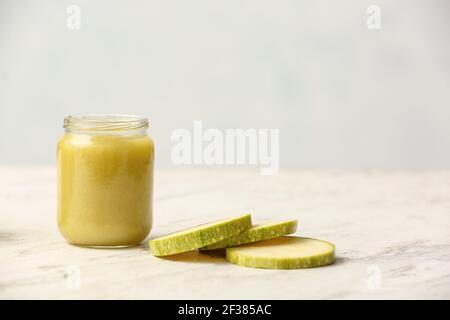 Jar with healthy baby food and zucchini on light background Stock Photo
