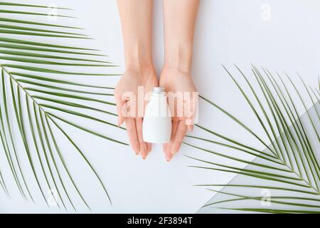 Female hands with cosmetic product and tropical leaves on light background Stock Photo