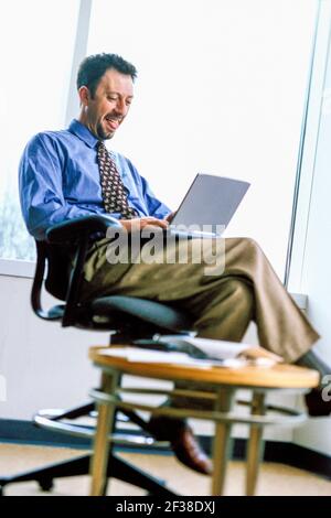 Businessman laughing while working on laptop computer. Stock Photo