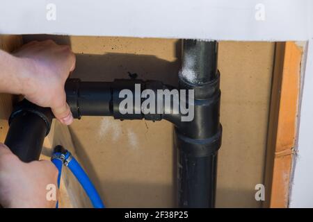 Plumber hands in glue two pieces of plastic drains pipe, close up on new bathroom Stock Photo