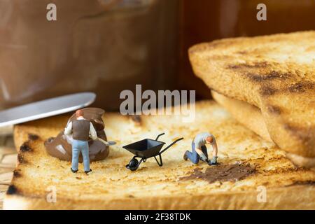 Miniature people are spreading chocolate on toast. Stock Photo