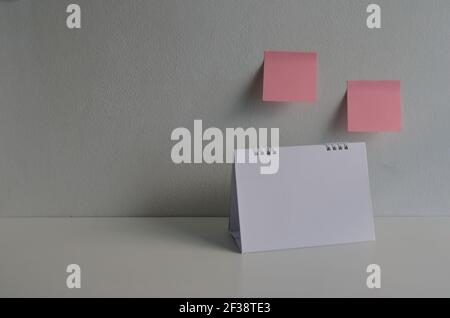 Closeup and selective focus on blank desk calendar standing on wooden table against empty sticky notes on cement wall Stock Photo