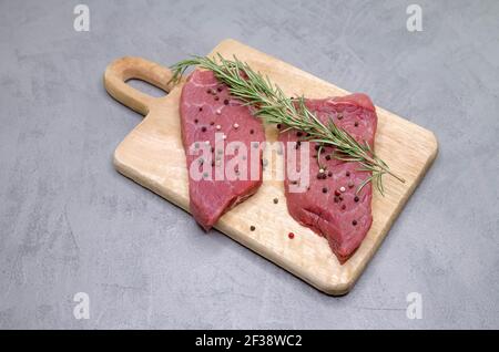 Raw beef steak with spices and rosemary on gray background Stock Photo