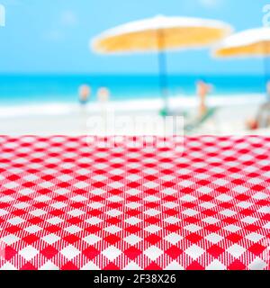 Red checkered table cloth on blurred beach background, summer holiday beach picnic concept - can be used for display or montage your products Stock Photo