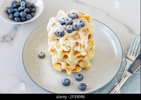 Belgian waffles with blueberries on the light barble table served with milk. Healthy breakfast Stock Photo