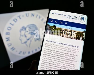 Person holding cellphone with website of German university Humboldt-Universität zu Berlin on screen in front of logo. Focus on phone display. Stock Photo