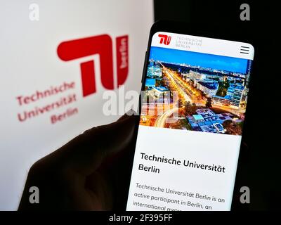 Person holding cellphone with webpage of German university Technische Universität Berlin on screen in front of logo. Focus on center of phone display. Stock Photo